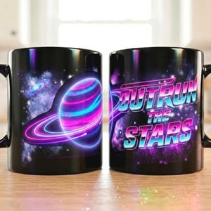 May include: A black ceramic mug featuring a vibrant space-themed graphic. One side displays a glowing planet with rings in shades of neon pink and blue against a starry nebula. The other side features the text "OUTRUN THE STARS" in a bold, retro-style font.