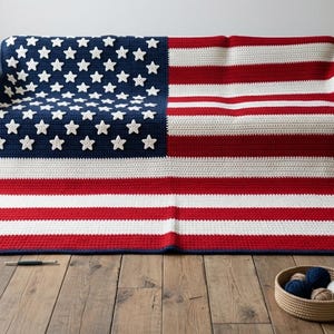 May include: A rectangular crochet blanket featuring the design of the American flag with red, white, and blue yarn. The blanket displays a blue field with white stars and alternating red and white horizontal stripes, finished with a dark blue border.