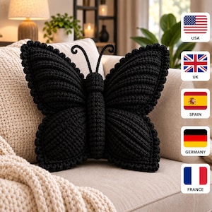 May include: A black butterfly-shaped throw pillow crafted with a textured crochet knit pattern. The pillow features a central body section, two large symmetrical wings with scalloped edges, and two thin, curved antennae extending from the top.