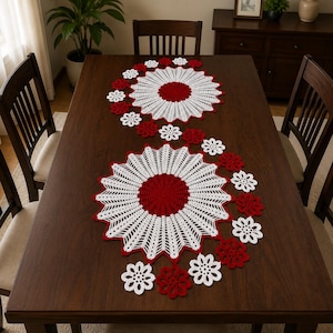 May include: A crochet table runner featuring two large circular motifs with solid red centers and white radiating patterns, connected by a winding trail of smaller red and white flower-shaped crochet pieces arranged in an S-curve across the surface.