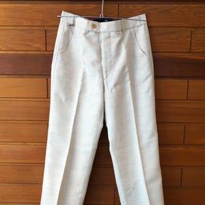 Peut inclure: Pantalon blanc cassé doté d'un tissage texturé subtil avec de petites taches sombres. Le vêtement présente une ceinture structurée avec un bouton central unique, une braguette zippée, deux poches latérales et une coupe droite épurée.