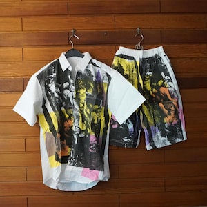 Könnte beinhalten: Ein Set aus einem kurzärmeligen Hemd mit Knopfleiste und passender Shorts auf weißer Basis mit einem auffälligen, abstrakten Grafikdruck in Schwarz, Gelb und Pink. Das Hemd hat einen klassischen Kragen und die Shorts einen elastischen Bund.