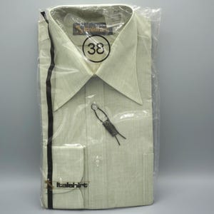 May include: A light green long-sleeve button-down shirt with a pointed collar, packaged in a clear plastic bag. The shirt features the brand name Italshirt, a size 38 label, and a small black tag attached to the front button placket.