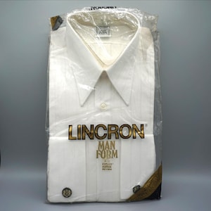 May include: A crisp white long-sleeve dress shirt with a pointed collar, packaged in a clear plastic bag. The shirt features the brand name Lincron and the text Man Form printed in gold on the front, along with two dark circular cuff buttons.
