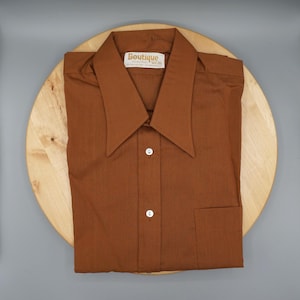 Op de afbeelding: Een effen bruin overhemd met lange mouwen, een brede puntkraag en een enkele borstzak. Het label in de nek aan de binnenzijde bevat de tekst Boutique. Het overhemd is aan de voorzijde voorzien van twee zichtbare witte knopen.