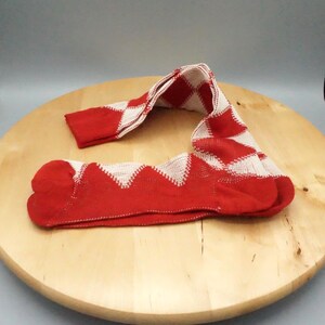 Może przedstawiać: Para skarpet w czerwono-biały wzór w romby. Skarpety wykonane są z dzianiny i posiadają powtarzający się geometryczny wzór czerwonych rombów z białym obrysem, rozciągający się od palców aż po ściągacz znajdujący się na górze skarpety.