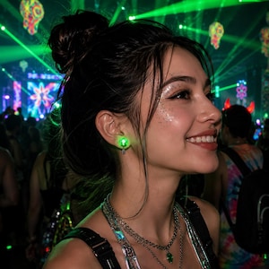 Pode incluir: Um brinco de pino LED verde brilhante com um design de esfera redonda e translúcida. O brinco é usado no lóbulo da orelha e emite uma luz verde vibrante e luminosa, contrastando com o ambiente festivo e escuro visível ao fundo.