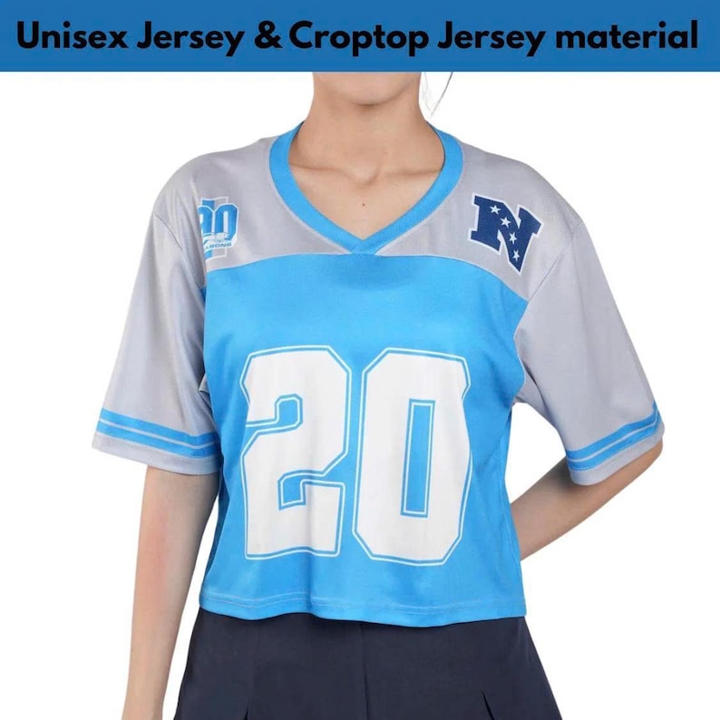Op de afbeelding: Een shirt met V-hals, een lichtblauw middenpaneel met het grote witte nummer 20, grijze mouwen met blauwe strepen en een donkerblauwe letter N met witte sterren op de borst. De tekst Unisex Jersey & Croptop Jersey material is zichtbaar.