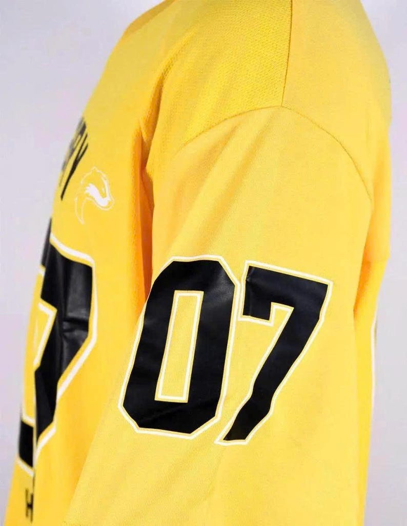 Op de afbeelding: Een felgeel shirt met lange mouwen voorzien van het nummer 07 in grote zwarte cijfers met een witte omlijning op de mouw. De stof heeft een textuur met een mesh-uiterlijk en een gedeeltelijk wit grafisch logo is zichtbaar op de borst.