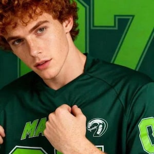 Op de afbeelding: Een donkergroen shirt met V-hals en de tekst MALFOY in limoengroene letters op de borst. Het shirt is voorzien van een limoengroen slangenembleem en het nummer 07 in limoengroen met een witte omlijning op de voorzijde en de mouw.
