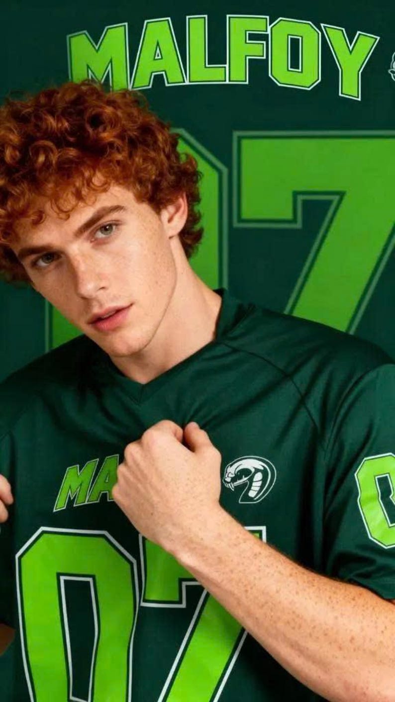 Op de afbeelding: Een donkergroen shirt met V-hals en de tekst MALFOY in limoengroene letters op de borst. Het shirt is voorzien van een limoengroen slangenembleem en het nummer 07 in limoengroen met een witte omlijning op de voorzijde en de mouw.