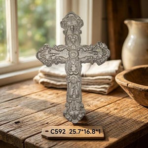 Może przedstawiać: Srebrzysty metalowy krzyż z misternymi tłoczonymi zawijasami i kwiatowymi detalami. Mała drewniana etykieta u podstawy zawiera tekst C592 25.7*16.8*1, wskazujący wymiary przedmiotu w centymetrach.