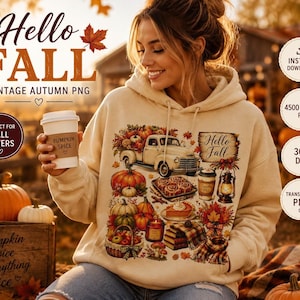 Puede incluir: Una sudadera con capucha de color beige que presenta un estampado gráfico de un camión antiguo, calabazas, una linterna, una cesta de manzanas y un trozo de tarta. El texto en el gráfico dice Hello Fall. La sudadera tiene mangas largas.