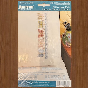 May include: A Janlynn stamped cross stitch pillowcase pair kit, #021-1003 Patchwork Butterfly. The packaging displays a white fabric with a vertical row of five colorful butterflies in yellow, red, pink, and blue, alongside a blue decorative border.
