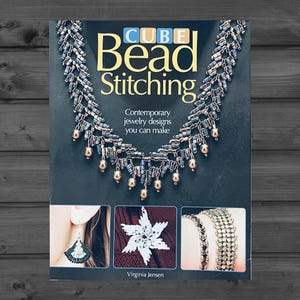 May include: A book titled Cube Bead Stitching by Virginia Jensen with a dark cover featuring a beaded necklace with metallic grey and gold beads. The cover includes three smaller images showing a beaded earring, a star ornament, and two bracelets.