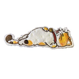 May include: An embroidered patch featuring a white calico cat lying on its side with orange and brown spots. The cat has a red collar with a small gold bell, closed eyes, and a small blue teardrop near its face, rendered in detailed thread work.