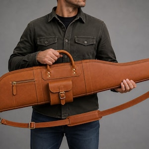 Può includere: Una custodia lunga per fucile in pelle color cuoio dotata di maniglia superiore, tracolla rimovibile con sezione imbottita, una piccola tasca laterale con cerniera e una tasca frontale con chiusura a fibbia, rifinita con dettagli in ottone.