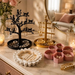 May include: A black cat-themed tree jewellery stand, a gold cat-topped jewellery rack, a white flower-shaped jewellery tray, a pink lotus-shaped jewellery box, and a gold pearl hair clip. These items are arranged on a marble surface for jewellery storage.