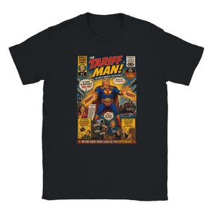 May include: A black short-sleeve t-shirt featuring a graphic print of a comic book cover titled The Tariff Man. The artwork depicts a superhero figure in a blue and red costume with a cape, surrounded by various speech bubbles and comic panels.