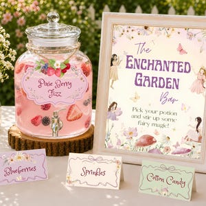 May include: A glass beverage dispenser filled with pink liquid and berries, featuring a label reading Pixie Berry Fizz. Next to it is a framed sign titled The Enchanted Garden Bar, with three small tent cards labeled Blueberries, Sprinkles, and Cotton Candy.
