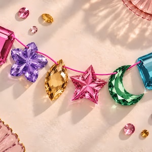 May include: A string of faceted crystal beads in various shapes including a pink rectangle, purple flower, amber marquise, pink star, green crescent moon, and blue rectangle, all threaded on a bright pink cord with matching loose crystals.
