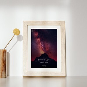 K&ouml;nnte beinhalten: Ein rechteckiger Rahmen aus hellem Holz mit einem vertikalen Druck einer dunklen Bergsilhouette vor einem violetten und roten Sternenhimmel. Der Druck enth&auml;lt den Text Olivia & Noah, The day we met, 18.04.2022 und Austin, USA.