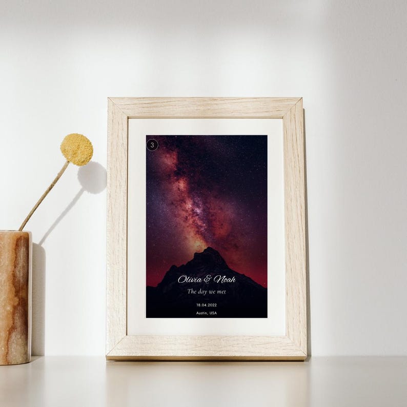 K&ouml;nnte beinhalten: Ein rechteckiger Rahmen aus hellem Holz mit einem vertikalen Druck einer dunklen Bergsilhouette vor einem violetten und roten Sternenhimmel. Der Druck enth&auml;lt den Text Olivia & Noah, The day we met, 18.04.2022 und Austin, USA.