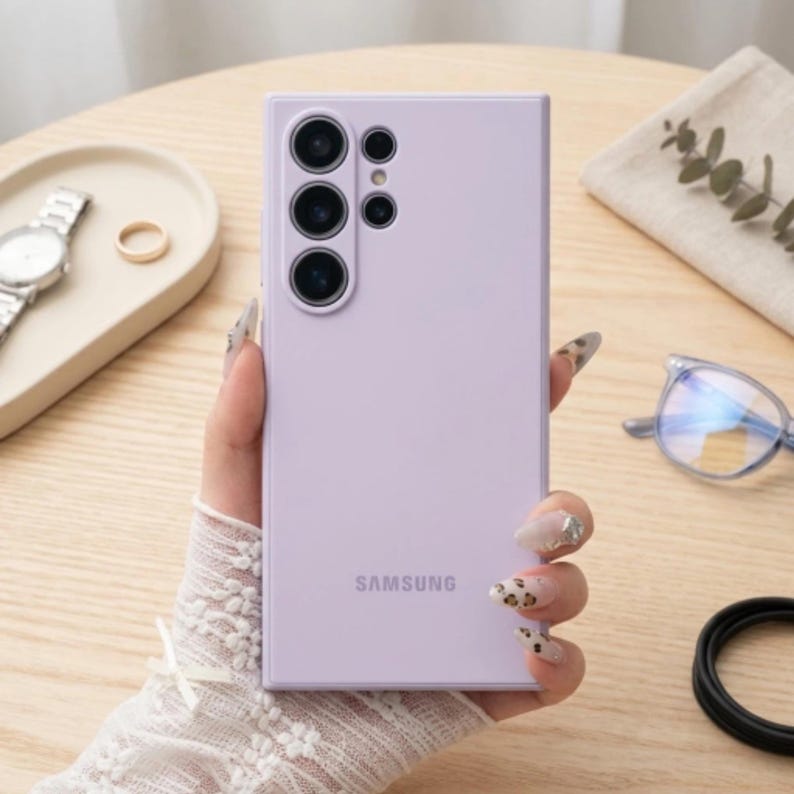 May include: A light lavender Samsung smartphone with a rectangular body and a multi-lens camera array on the back. The device features a smooth, matte finish and the Samsung logo printed in a subtle, darker shade near the bottom center.