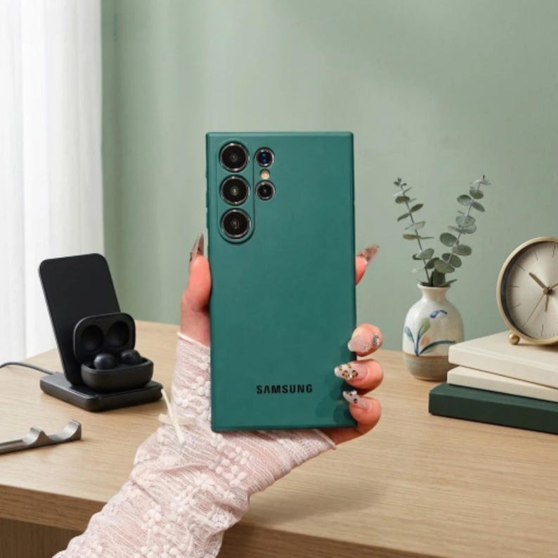May include: A dark green smartphone case with a matte finish, featuring a cutout for the camera array and the Samsung logo printed in black at the bottom. The case is designed for a rectangular device with rounded corners and a flat back surface.