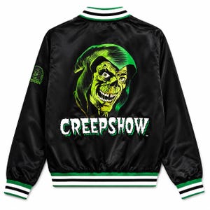 Puede incluir: Una chaqueta universitaria de satén negro con un gráfico verde de una figura con capucha y calavera en la espalda sobre el texto blanco CREEPSHOW. La chaqueta tiene cuello, puños y dobladillo acanalados con rayas negras, blancas y verdes.