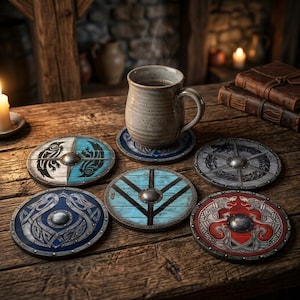 Op de afbeelding: Een set van vijf ronde onderzetters ontworpen als miniatuur houten schilden, elk voorzien van een centrale metalen knop en verschillende beschilderde patronen, waaronder op Noorse wijze geïnspireerde diermotieven, geometrische lijnen en blauwe, rode en grijze tinten.