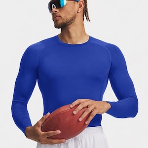 May include: A royal blue long-sleeve compression shirt with a crew neckline and raglan sleeves. The shirt is made of a smooth, form-fitting fabric. The garment is worn with white athletic shorts and paired with blue and white sports sunglasses.