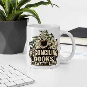 May include: A white ceramic mug featuring a graphic of a coffee cup, a calculator, and financial ledger sheets. The text reads RECONCILING BOOKS. NOT MY CAFFEINE INTAKE. The design uses shades of green, black, and tan on the mug's exterior surface.