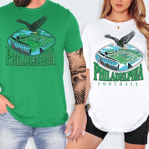 two people wearing Philadelphia Football t-shirts, one in a green shirt and the other in a white shirt.