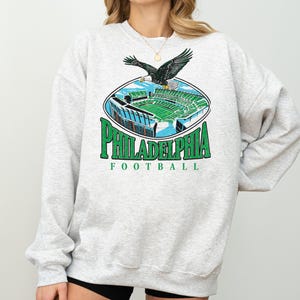 A gray sweatshirt with a graphic design depicting a Philadelphia Eagles football stadium and an eagle in flight.
