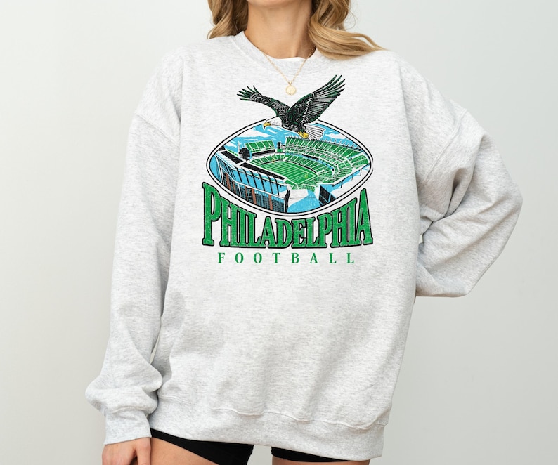 A gray sweatshirt with a graphic design depicting a Philadelphia Eagles football stadium and an eagle in flight.