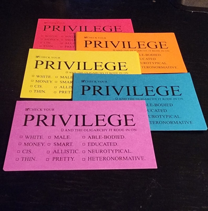 Puede incluir: Cinco tarjetas de &iacute;ndice de colores con la palabra "Privilege" impresa en negro. Cada tarjeta tiene una lista de verificaci&oacute;n de caracter&iacute;sticas, que incluyen "Blanco", "Masculino", "Con capacidad para trabajar", "Educado", "Neurot&iacute;pico" y "Heteronormativo". El texto "Y la oligarqu&iacute;a sobre la que cabalg&oacute;" est&aacute; impreso en cada tarjeta.