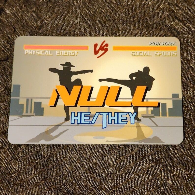 Puede incluir: Una ilustraci&oacute;n digital de un juego de lucha con dos siluetas de personas luchando. El juego se llama "NULL" y los personajes est&aacute;n etiquetados como "Energ&iacute;a f&iacute;sica" y "Cucharas sociales". El texto "HE/THEY" se muestra debajo del t&iacute;tulo del juego.