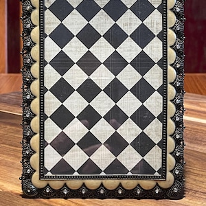 May include: A rectangular picture frame featuring a black and white diamond pattern insert. The frame has a scalloped cream-colored border accented with small clear rhinestones and an outer dark metal filigree edge with a beaded inner trim.
