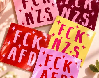 Könnte beinhalten: Fünf quadratische Aufkleber mit glänzender Oberfläche, die jeweils den Text FCK NZS oder FCK AFD in fetter, serifenloser Schrift zeigen. Die Designs enthalten kleine vierzackige Sternsymbole, die um den Text herum verteilt sind, in verschiedenen Farbkombinationen wie Pink, Rot, Gelb und Dunkelrot.
