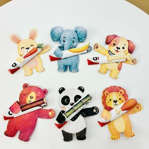 Puede incluir: Seis figuras de animales de papel troquelado que incluyen un conejo amarillo con una zanahoria, un elefante azul con un plátano, un perro marrón con un hueso, un oso rosa con un tronco, un panda blanco y negro con bambú y un león con un muslo de pollo.