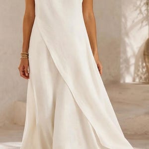 May include: A sleeveless, floor-length dress in a solid off-white color. The garment features a high, round neckline and a distinctive wrap-style front panel that creates an overlapping diagonal line, resulting in a flowing, flared skirt silhouette.