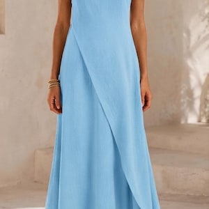 May include: A sleeveless light blue maxi dress featuring a round neckline and a distinctive overlapping wrap-style front panel that creates a diagonal line across the skirt, extending down to the floor in a simple, flowing, and unpatterned design.