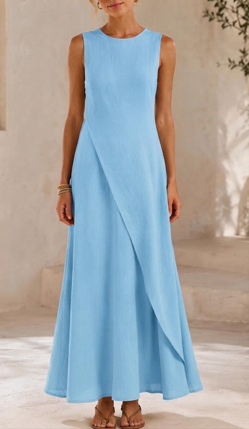 May include: A sleeveless light blue maxi dress featuring a round neckline and a distinctive overlapping wrap-style front panel that creates a diagonal line across the skirt, extending down to the floor in a simple, flowing, and unpatterned design.