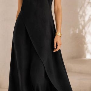 May include: A sleeveless black maxi dress featuring a high round neckline and a wrap-style front panel that creates a layered effect. The garment has a fitted bodice that transitions into a flowing, floor-length skirt with a subtle textured finish.