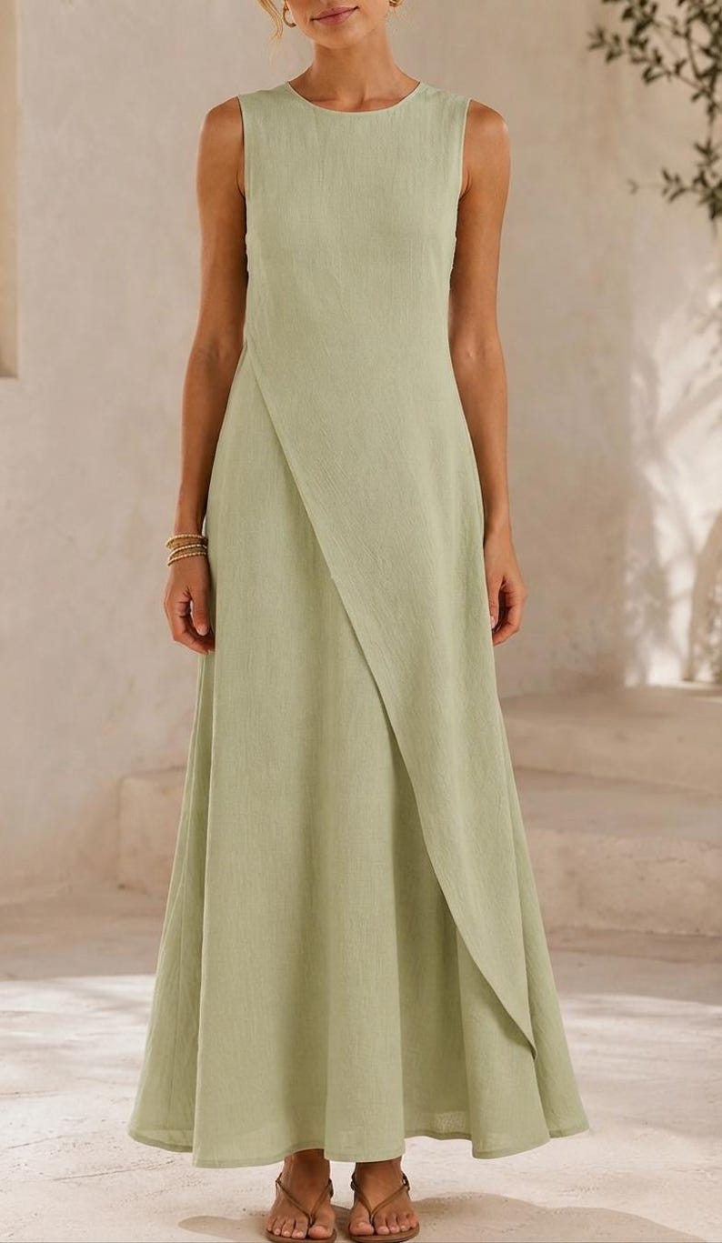 May include: A sleeveless sage green maxi dress featuring a round neckline and a distinctive overlapping front panel design that creates a diagonal hemline. The garment has a fitted bodice that transitions into a flowing, floor-length skirt silhouette.