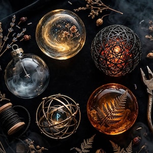 May include: A collection of decorative spheres including a clear glass ornament with smoke, a gold-flecked orb, a black geometric lattice ball, a gold wire cage sphere with a blue rune, an amber resin sphere with a fern, a spool of black cord, and pliers.