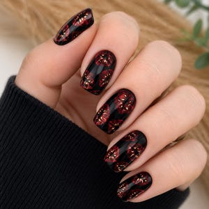 Pode incluir: Unhas pintadas com uma base preta brilhante com um padr&atilde;o repetitivo de pequenas marcas de l&aacute;bios em vermelho met&aacute;lico. As unhas t&ecirc;m um formato oval arredondado, exibindo um contraste vibrante entre o fundo escuro e a cor vermelha.