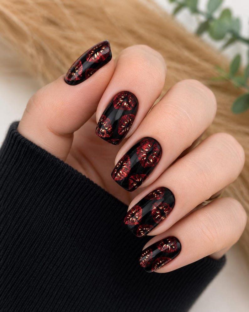 Pode incluir: Unhas pintadas com uma base preta brilhante com um padr&atilde;o repetitivo de pequenas marcas de l&aacute;bios em vermelho met&aacute;lico. As unhas t&ecirc;m um formato oval arredondado, exibindo um contraste vibrante entre o fundo escuro e a cor vermelha.