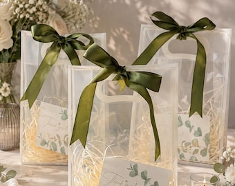 May include: Three clear plastic gift bags with die-cut handles, each tied with a dark olive green satin ribbon. Inside each bag is light-colored shredded paper filler and a rectangular card featuring a eucalyptus leaf design and the text Thank you!